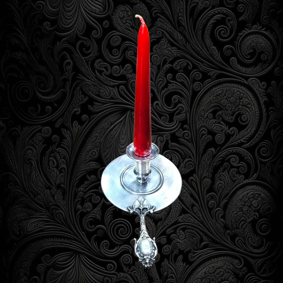 Palmatoria de Época en alpaca con vela roja sobre fondo barroco, ideal para añadir encanto vintage a tu hogar en decoración clásica.