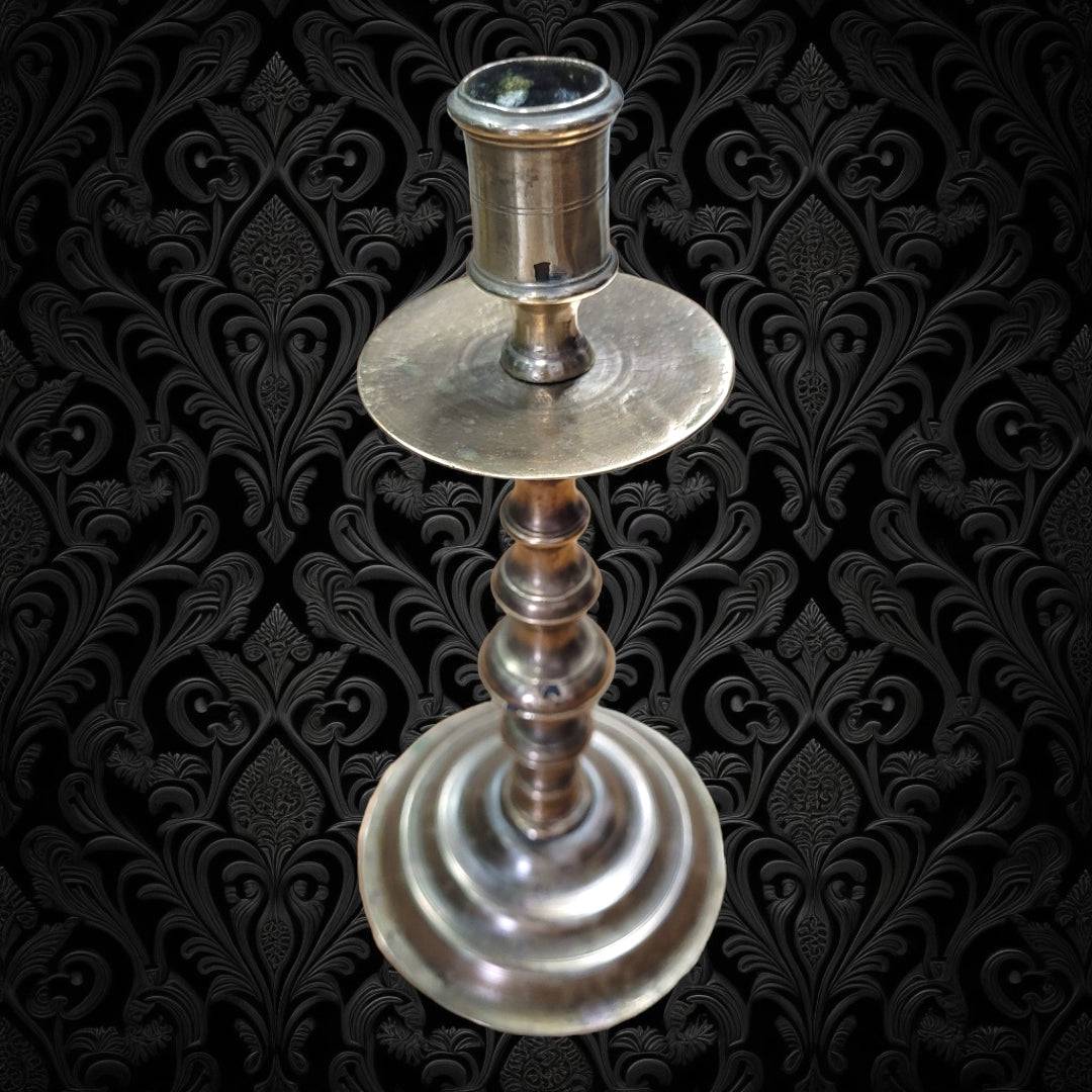 Candelero metal antiguo con diseño vintage sobre fondo decorativo negro. Candelabro elegante ideal para decoración clásica y sofisticada.