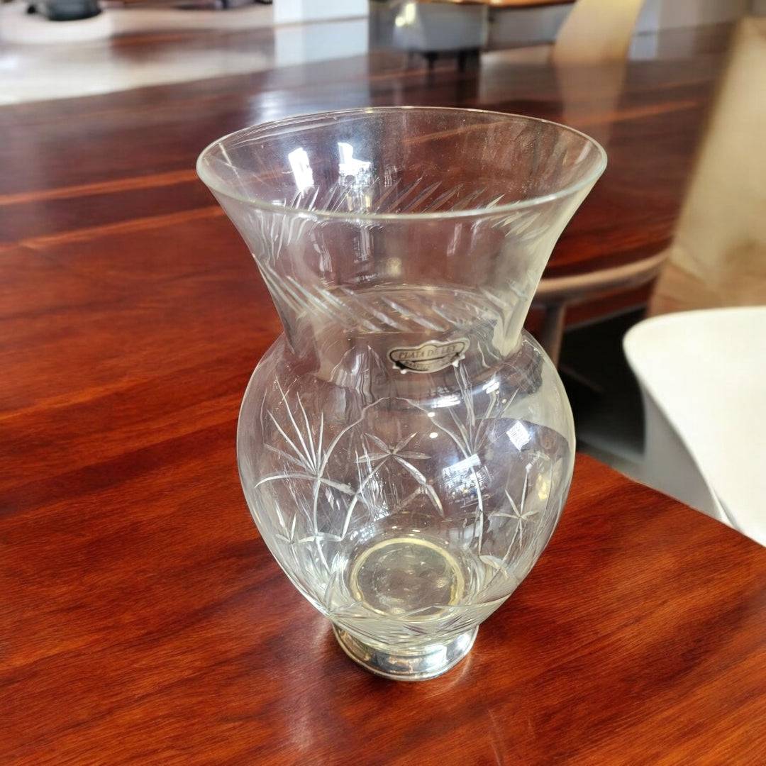 Jarrón de cristal tallado con pie de plata, estilo elegante, sobre mesa de madera en sala moderna. Ideal para decoración de interiores refinada.