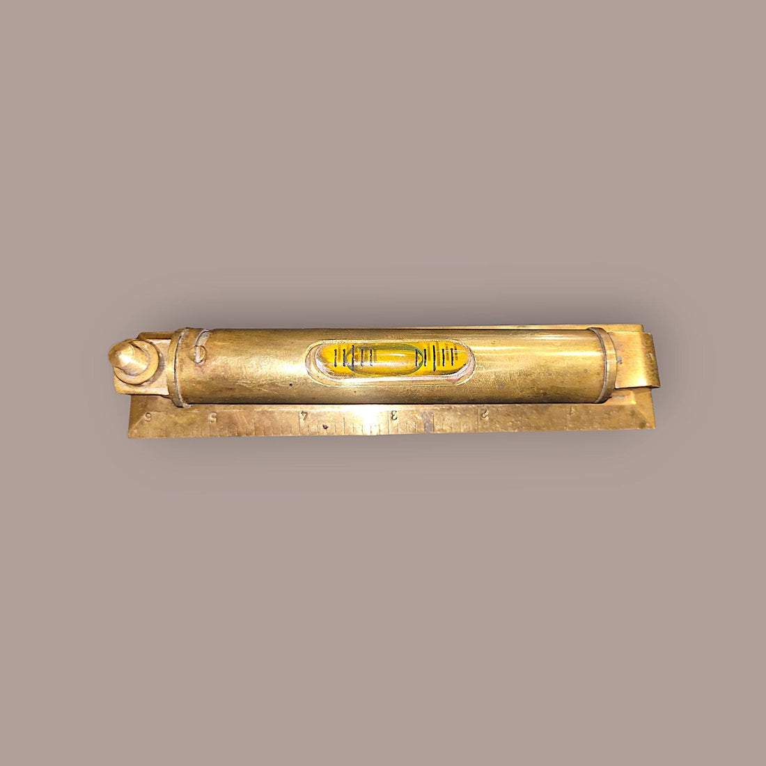 Nivel metálico con funda protectora de 14 cm en latón antiguo, base con escala grabada para mediciones precisas en decoración de interiores.
