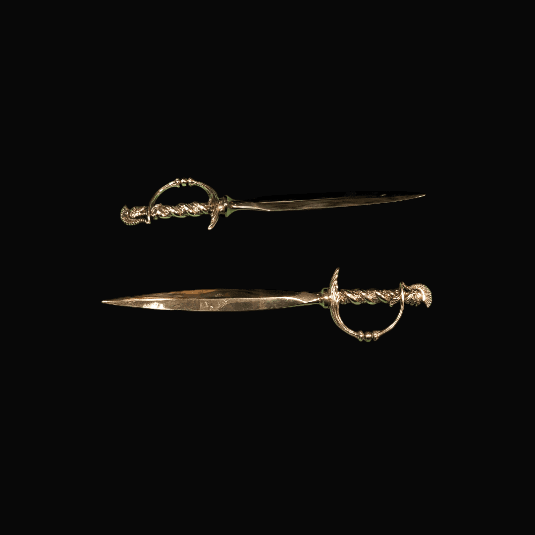 Pareja de abrecartas en forma de espadas de metal plateado cruzadas sobre fondo negro. Diseño elegante y funcional para escritorio.