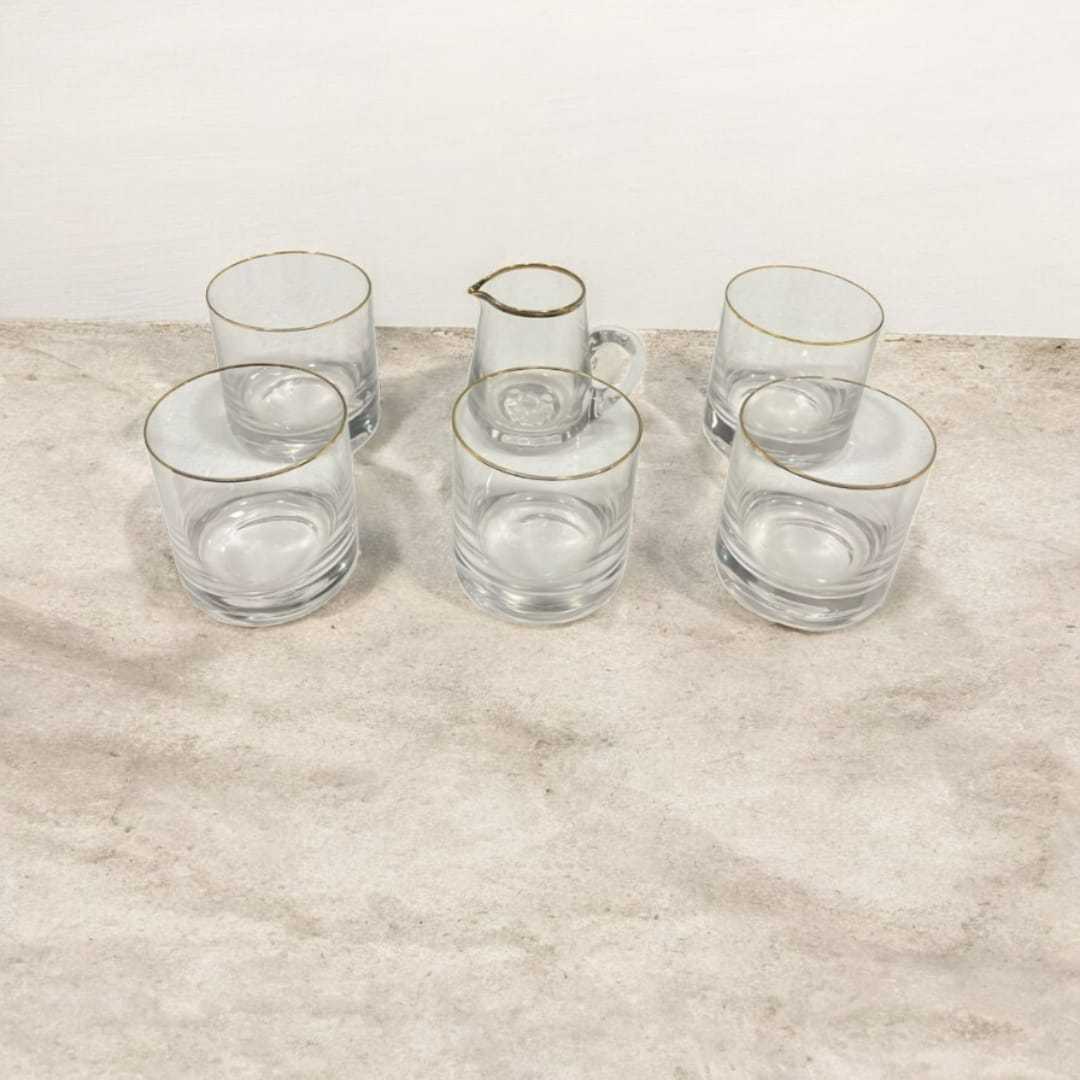 Conjunto de Cristal de Bohemia con filo de oro compuesto por jarra y 4 vasos sobre superficie de mármol. Ideal para decoración elegante en el hogar.