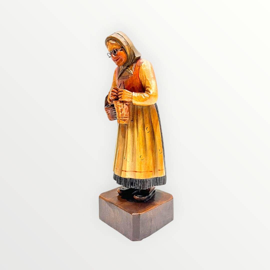Figura artesanal de mujer mayor con vestido tradicional y canastas, hecha en madera tallada. Perfecta para decoración rústica del hogar.