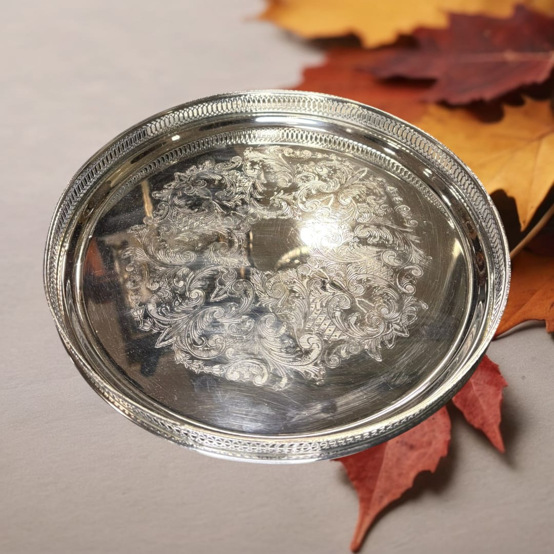 La bandeja redonda de metal plateada con rocallas decorativas es una pieza que combina funcionalidad y belleza atemporal