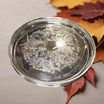 La bandeja redonda de metal plateada con rocallas decorativas es una pieza que combina funcionalidad y belleza atemporal