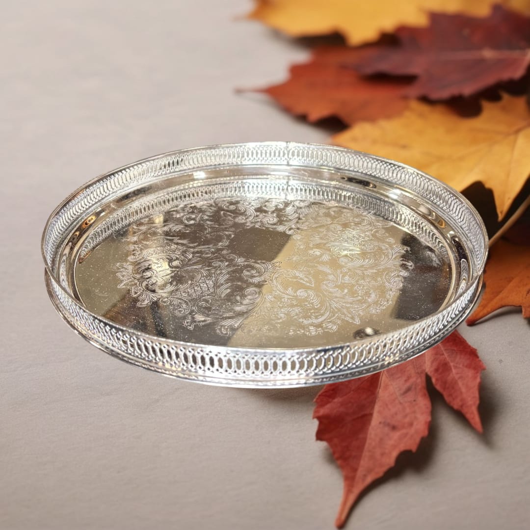 La bandeja redonda de metal plateada con rocallas decorativas es una pieza que combina funcionalidad y belleza atemporal