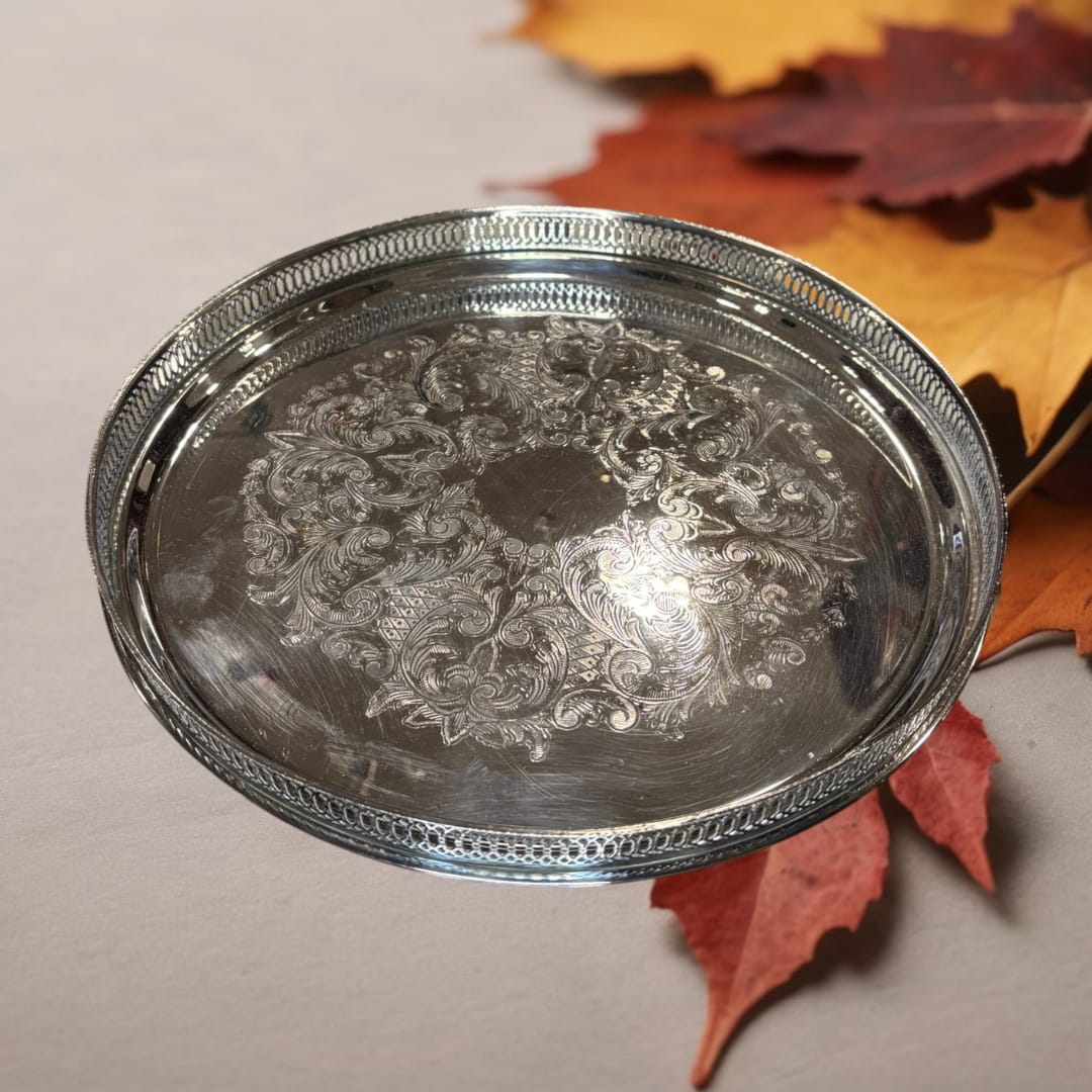 a bandeja redonda de metal plateada con rocallas decorativas está fabricada en metal plateado con acabado brillante, ofreciendo una superficie resistente y duradera.