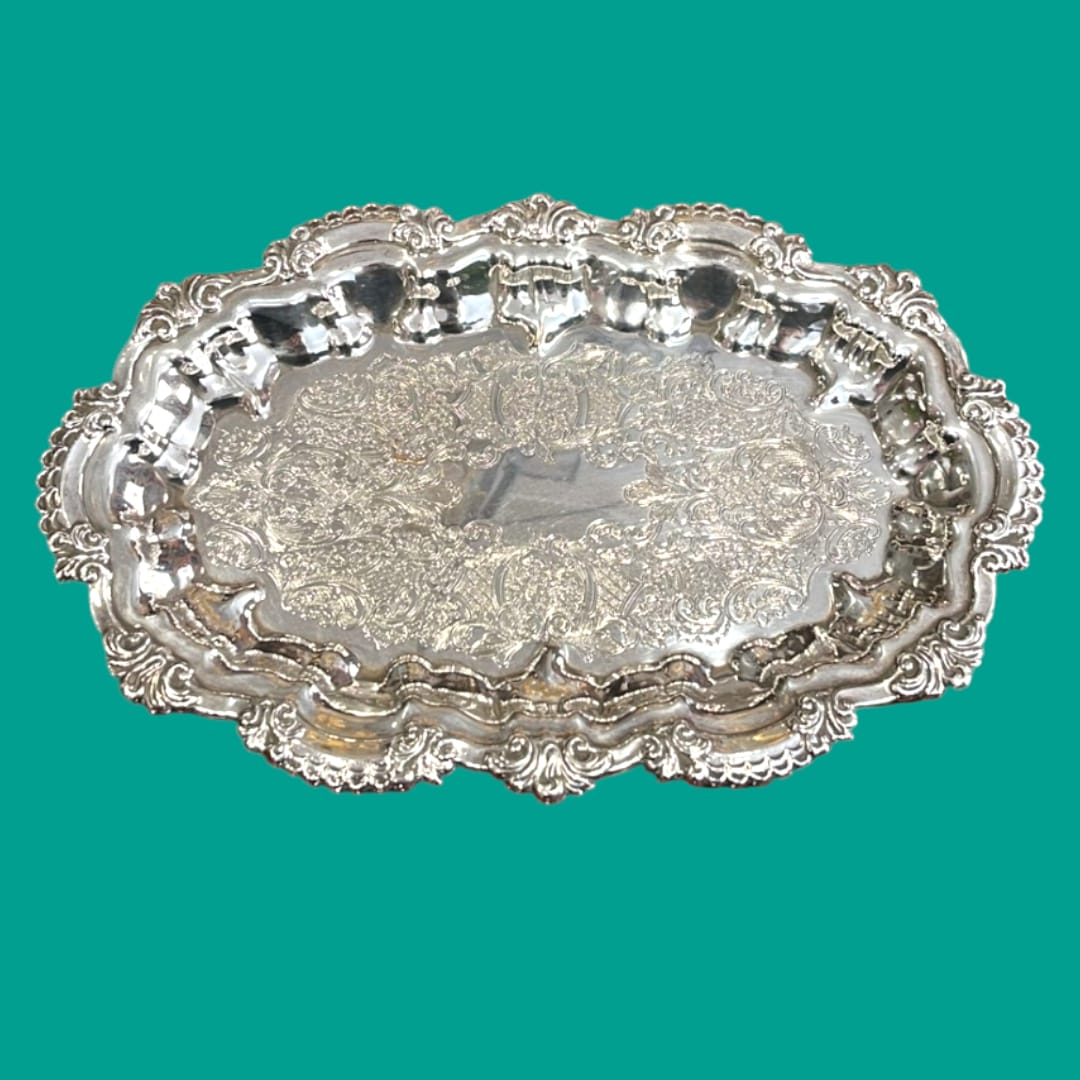 Bandeja de metal plateado con ornamentos detallados y bordes decorativos, ideal para decoración clásica en el hogar.