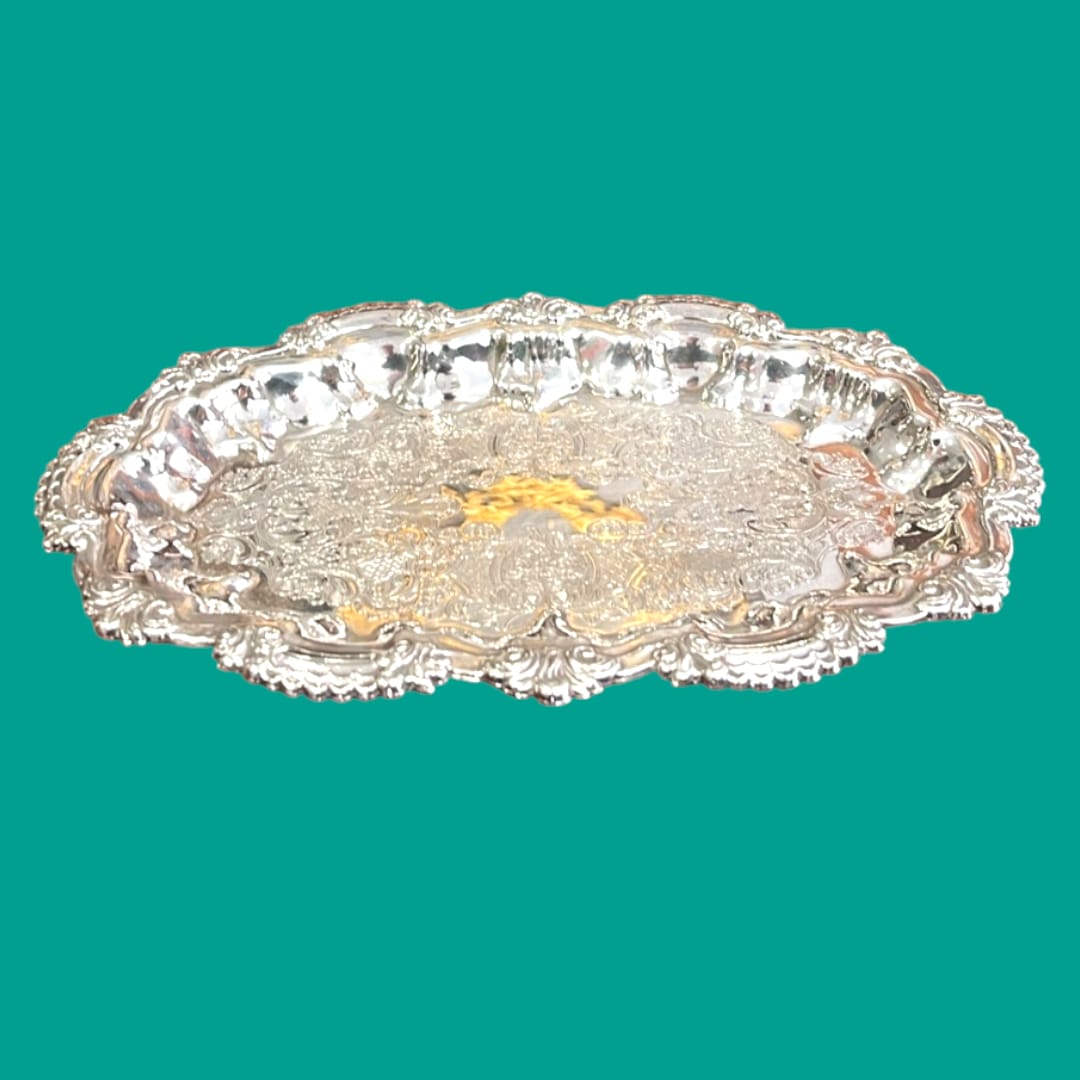 Bandeja de metal plateado con ornamentos detallados y bordes decorativos, ideal para decoración clásica en el hogar.