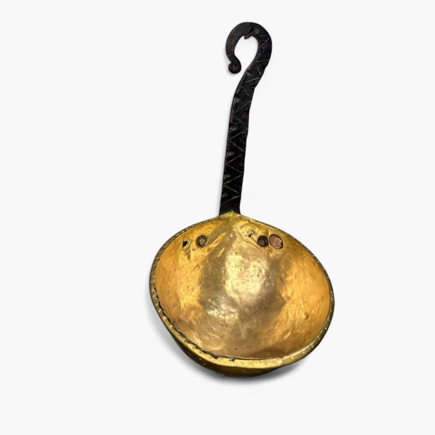 Vista superior del cazo antiguo de metal dorado con mango de hierro, destacando su diseño artesanal y valor como objeto decorativo.
