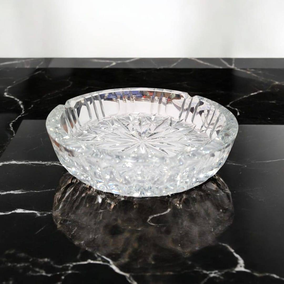 Cenicero de cristal con relieves en forma de estrellas sobre mesa de mármol negro, ideal para decoración elegante y funcional en el hogar.