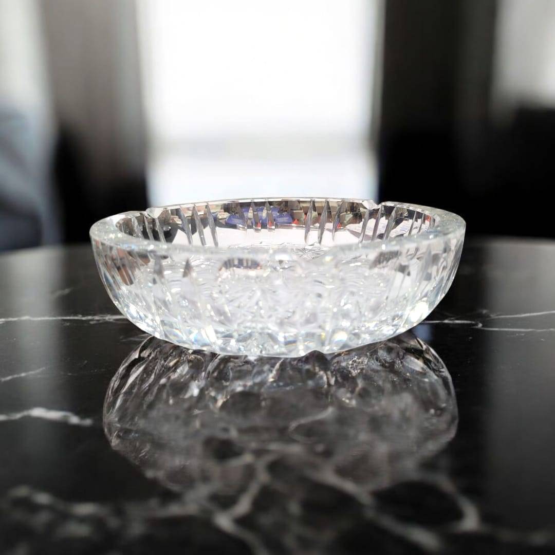 Cenicero de cristal con relieves en forma de estrellas sobre mesa de mármol negro, ideal para decoración elegante y funcional en el hogar.