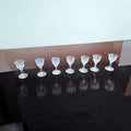 Siete copas de licor de cristal tallado antiguo alineadas sobre superficie negra, perfectas para coleccionistas y decoración elegante.