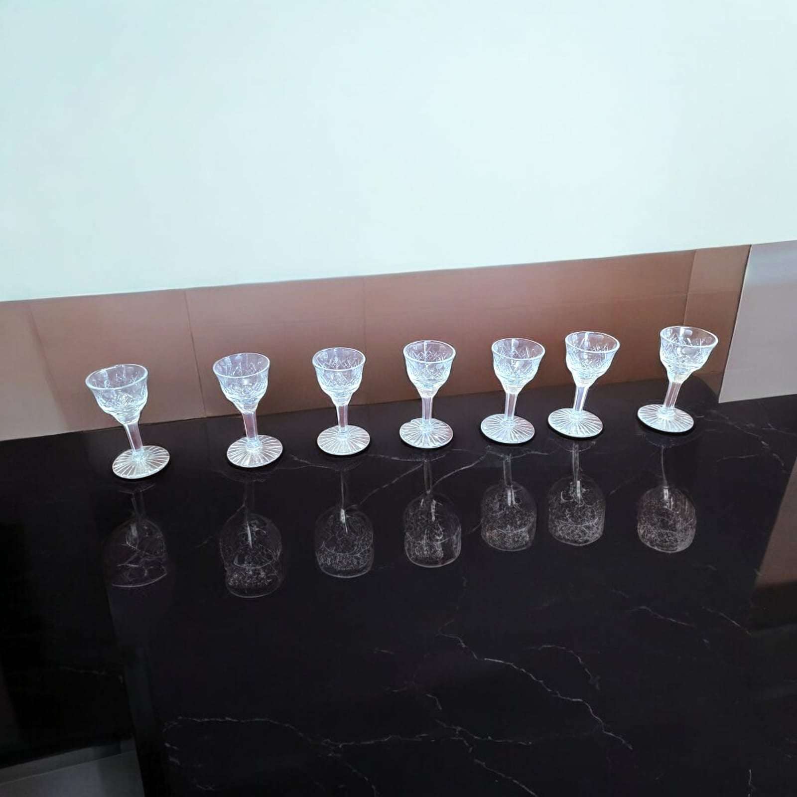 Siete copas de licor de cristal tallado antiguo alineadas sobre superficie negra, perfectas para coleccionistas y decoración elegante.