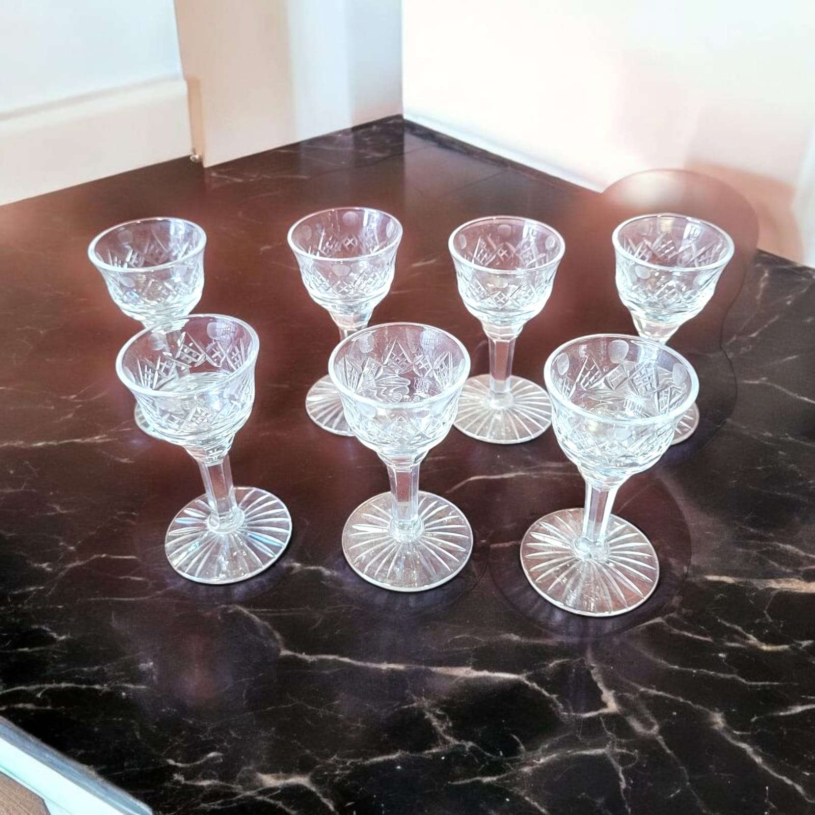 Juego de copas de licor de cristal tallado antiguo sobre mesa de mármol oscuro, diseño clásico ideal para decoración vintage.
