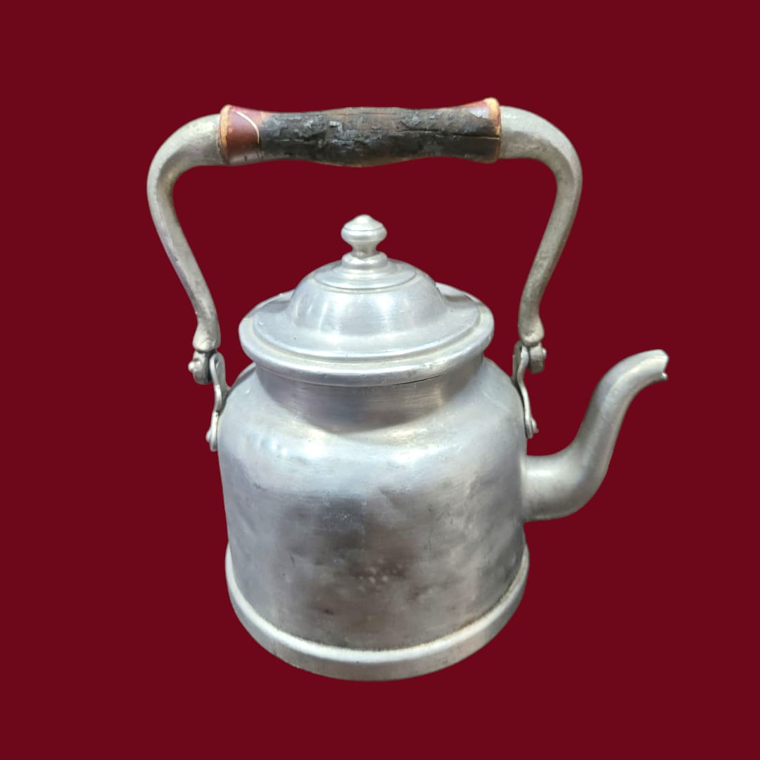 Cafetera de aluminio antigua con asa curva y tapa decorativa. Perfecta para aportar un toque vintage a la decoración del hogar o colección retro.