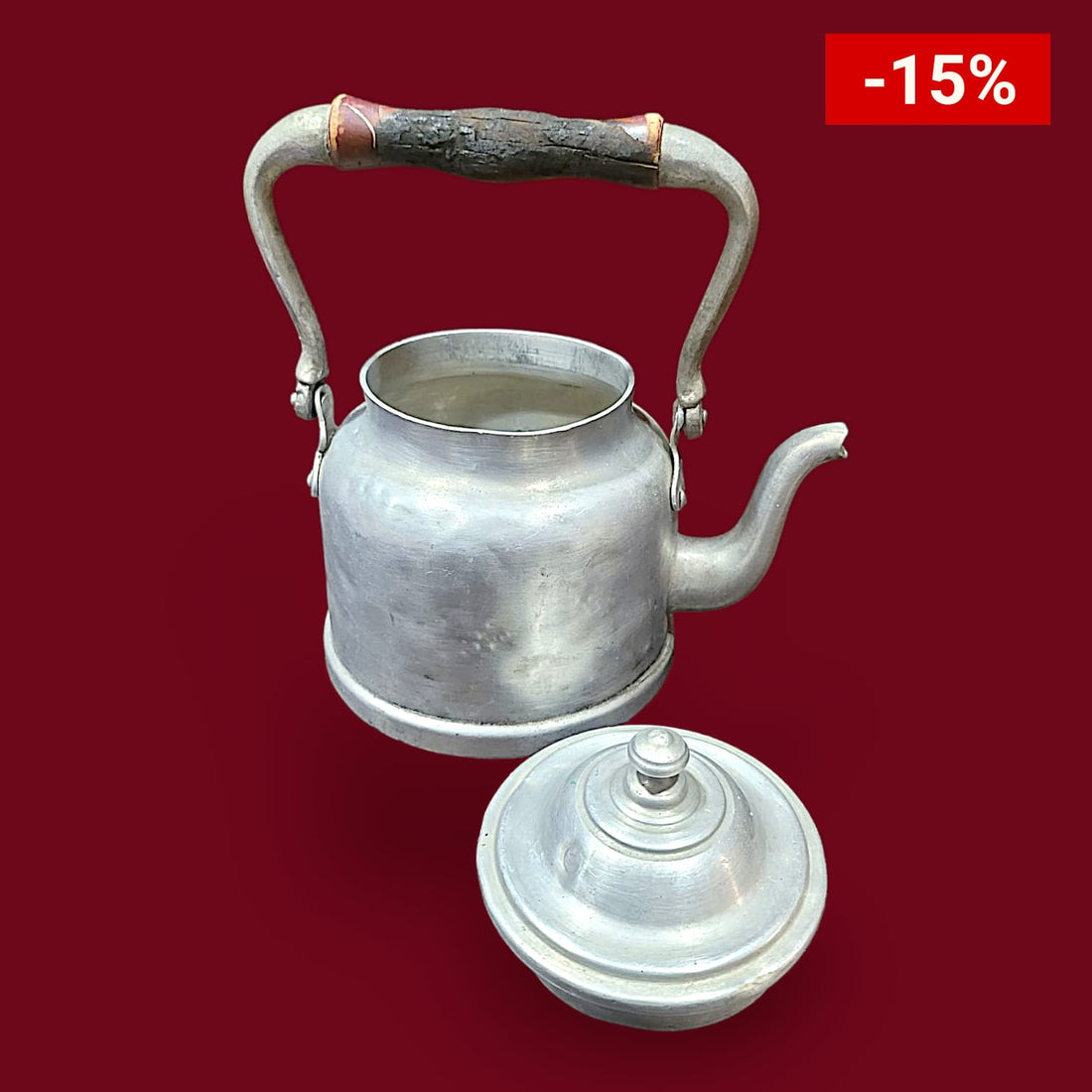 Cafetera de aluminio antigua con asa curva y tapa decorativa. Perfecta para aportar un toque vintage a la decoración del hogar o colección retro.