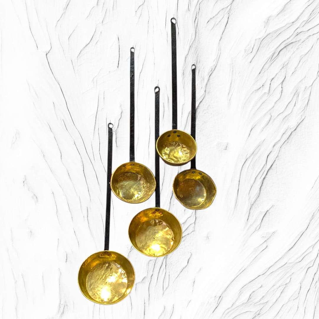 Cinco cazos antiguos con interior de metal dorado y mango de forja alineados verticalmente. Decoración única para hogar rústico.