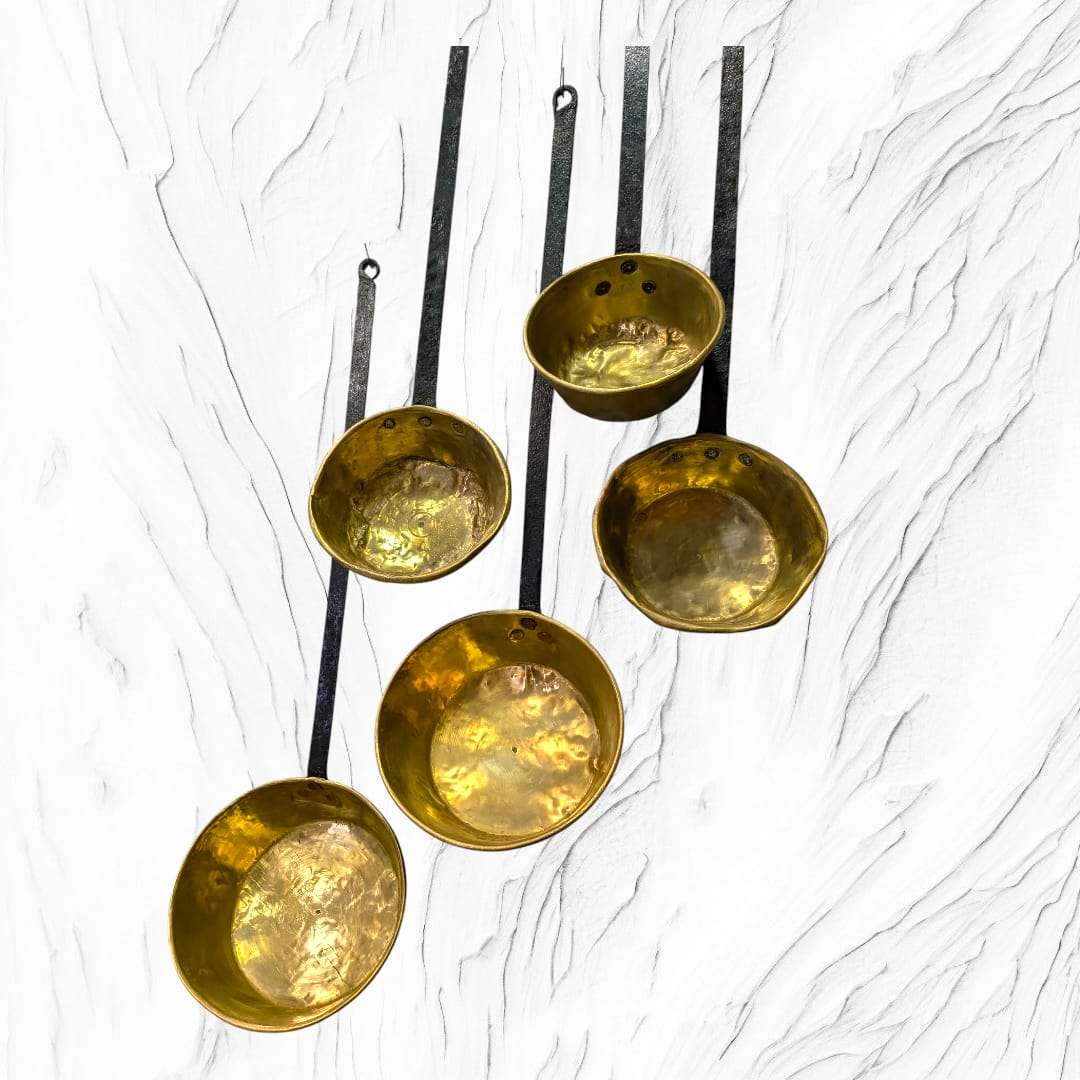 Cazos antiguos de metal dorado con mango de forja sobre fondo blanco. Lote decorativo ideal para ambientes clásicos o retro.