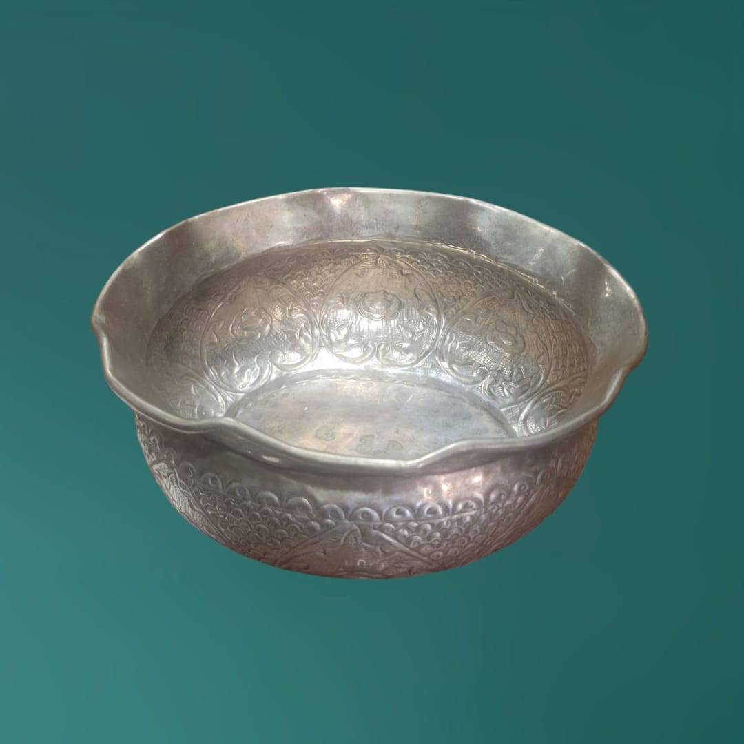 Frutero de metal plateado con bordes ondulados y grabado oriental, perfecto como centro de mesa decorativo.