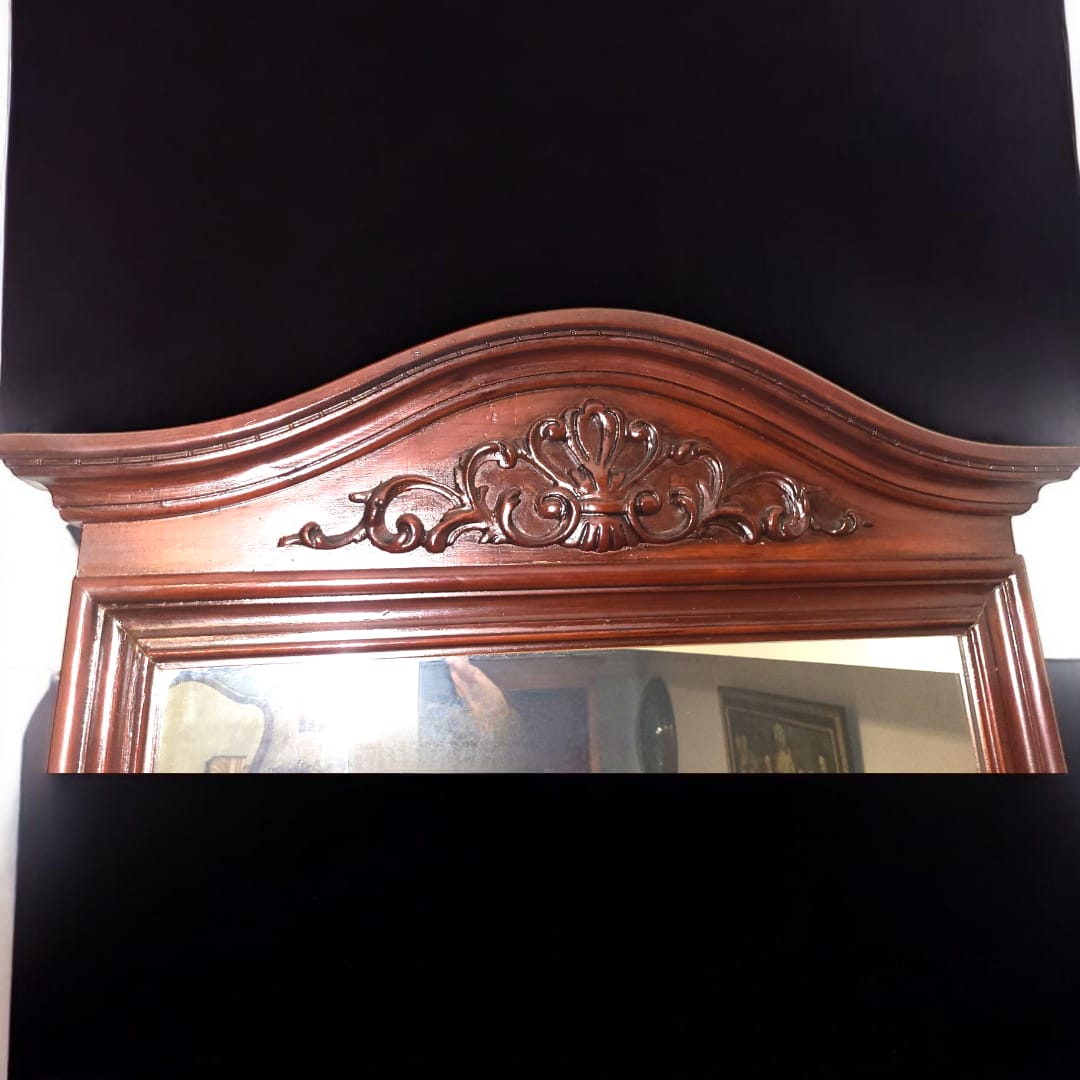 Vista detallada del tallado superior del espejo: "Espejo de caoba con detalles ornamentales tallados a mano. Elegancia en cada detalle."