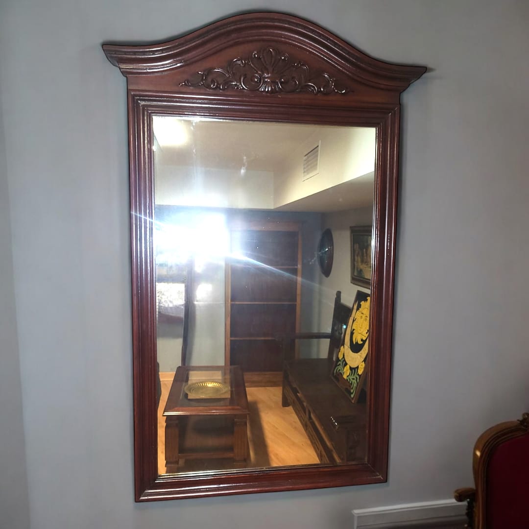 Vista detallada del tallado superior del espejo: "Espejo de caoba con detalles ornamentales tallados a mano. Elegancia en cada detalle."