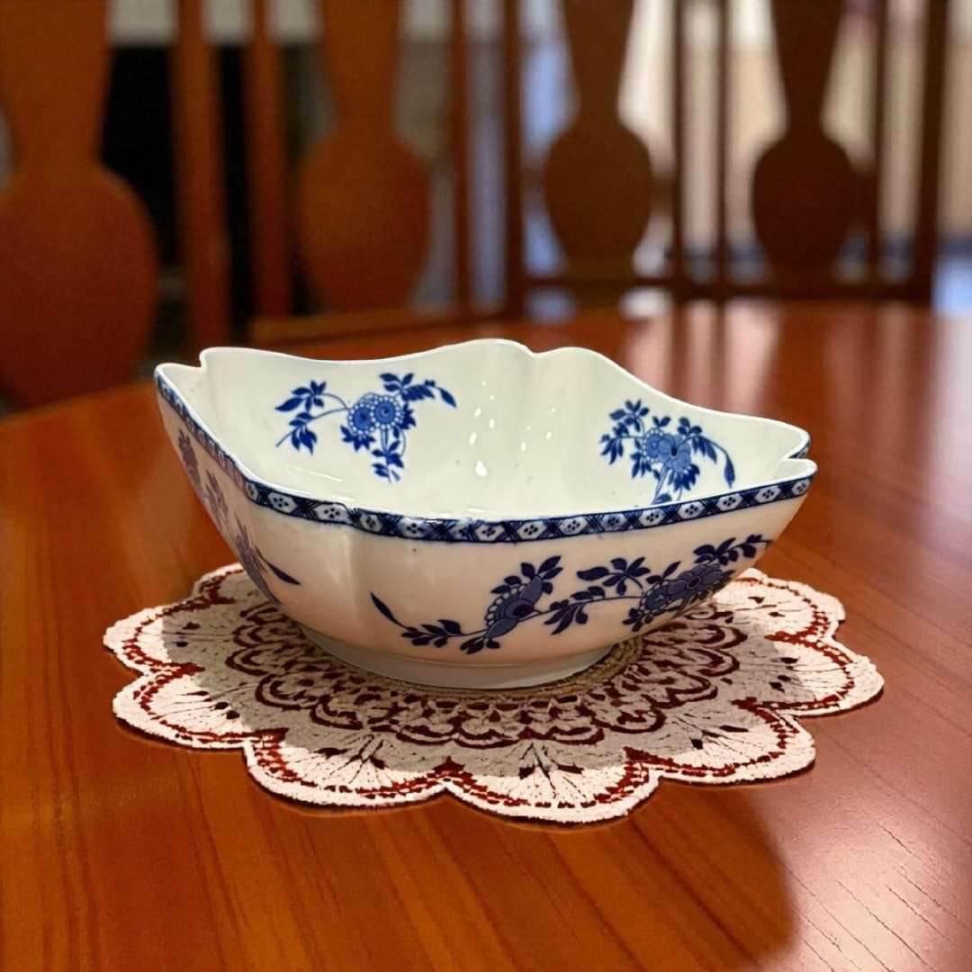 Frutero antiguo decorado con flores azules, sobre tapete de encaje.