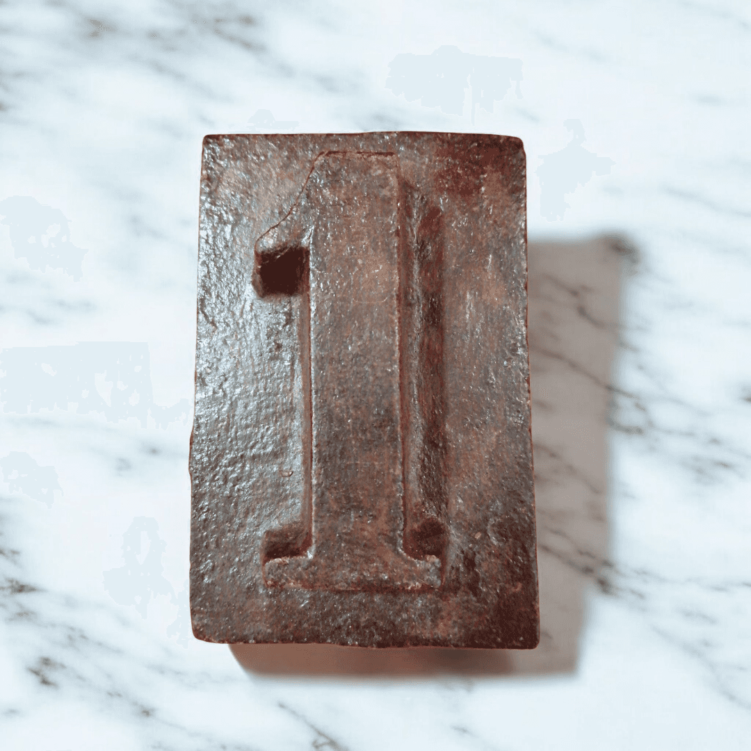 Numero 1 de hierro fundido vintage con acabado rústico sobre superficie de mármol. Decoracion unica para interiores o jardines.