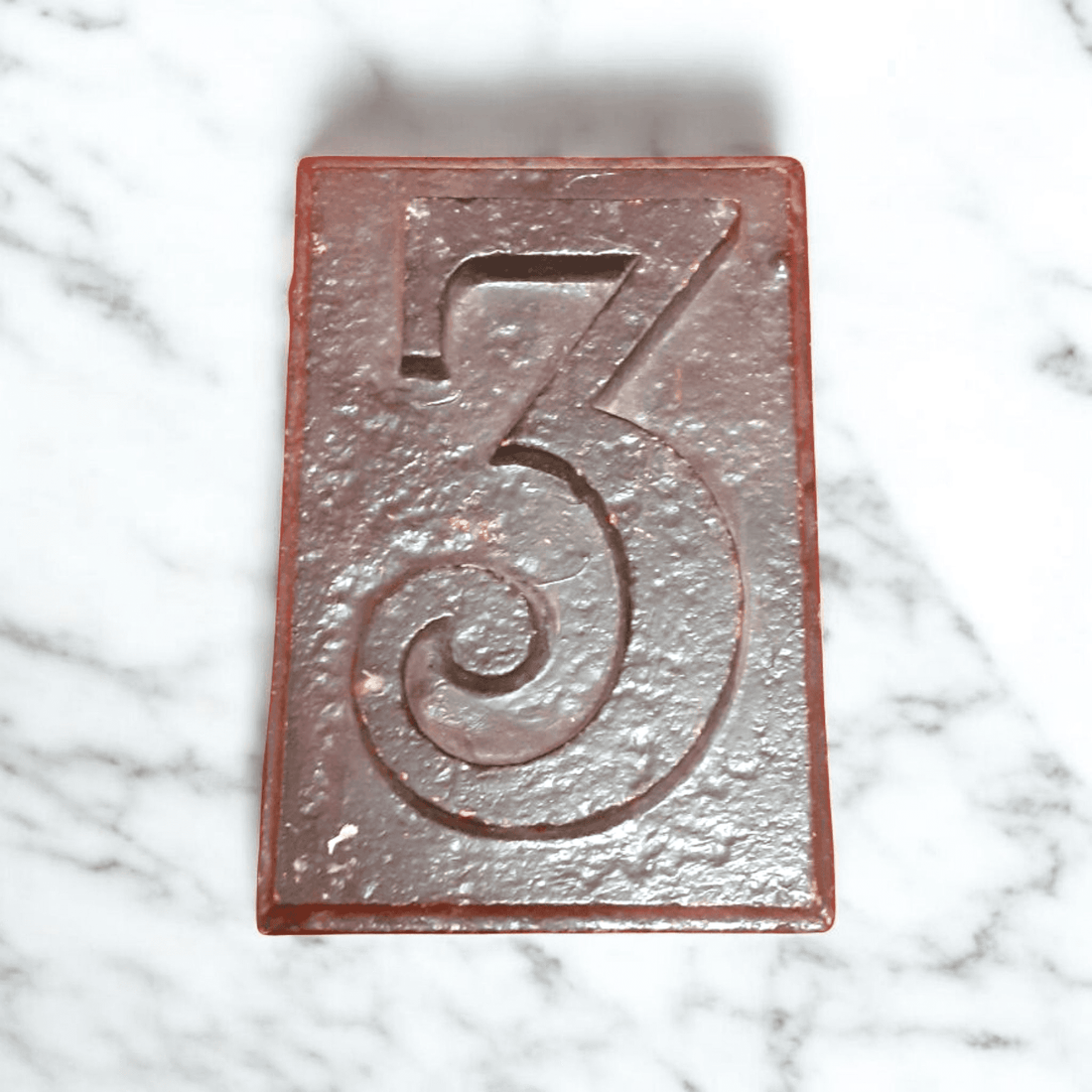 Número 3 de hierro fundido vintage con acabado rústico sobre fondo de mármol. Decoración única y resistente para exteriores o interiores.