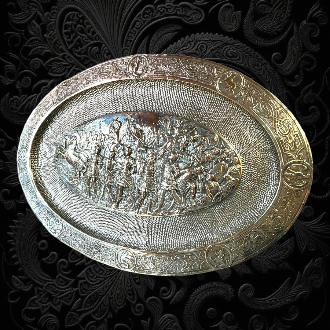 Bandeja decorativa ovalada en cobre plateado con diseño renacentista y escena de batalla en relieve. Ideal para añadir sofisticación al hogar.