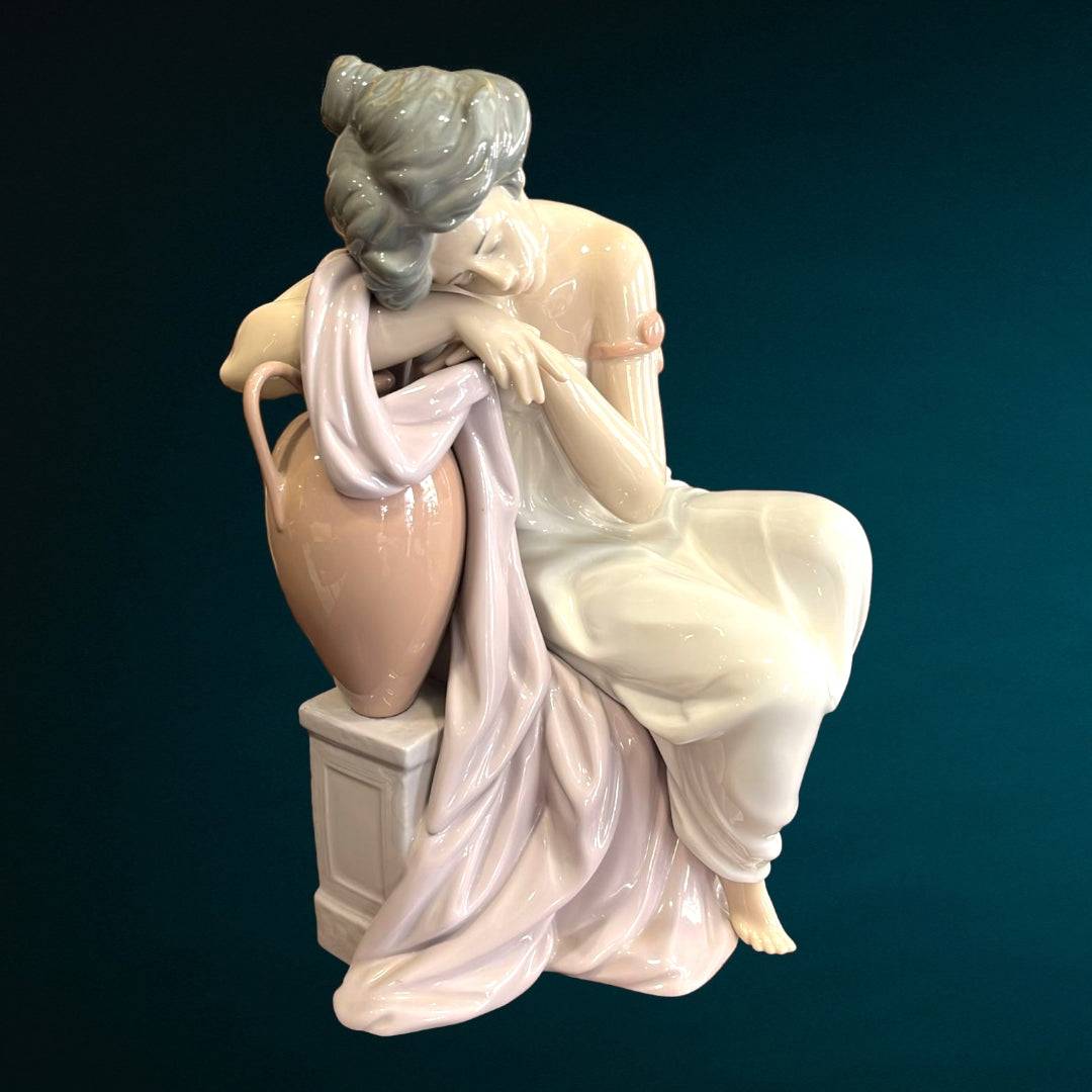 Figura Lladró 'Soñando Despierta' en porcelana fina, muestra a mujer recostada sobre ánfora con vestido blanco y rosa. Ideal para decoración elegante.