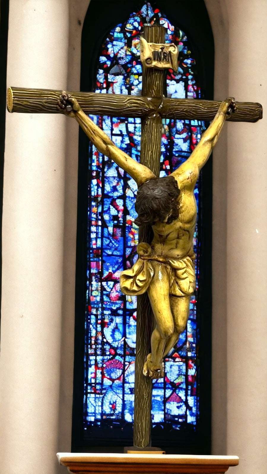Crucifijo de terracota con Cristo en cruz arbórea frente a vitral. Decoración religiosa para el hogar que transmite paz y devoción.