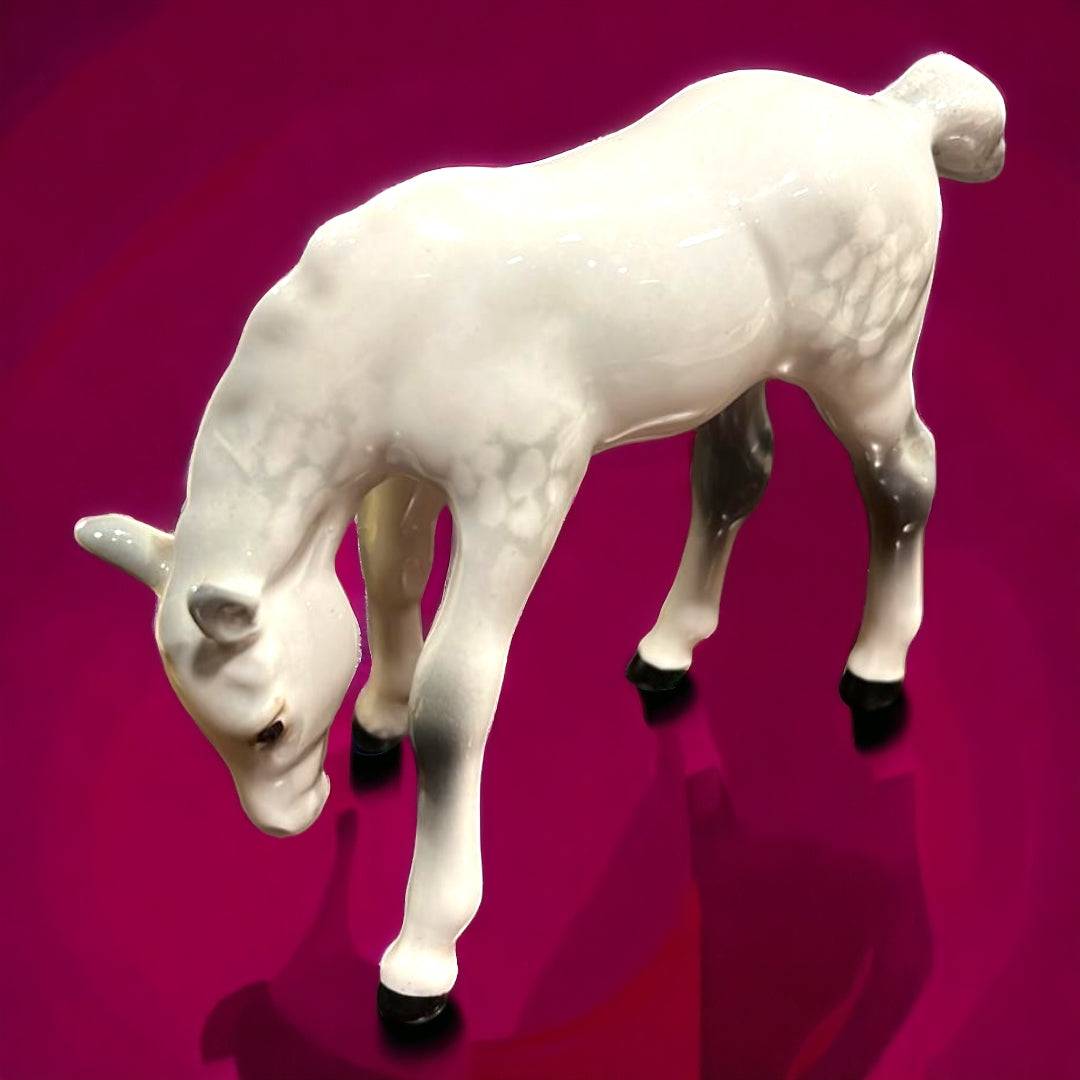 Caballo de porcelana Beswick en posición de pastar, acabado blanco brillante sobre fondo burdeos. Elegancia inglesa para coleccionistas de decoración.