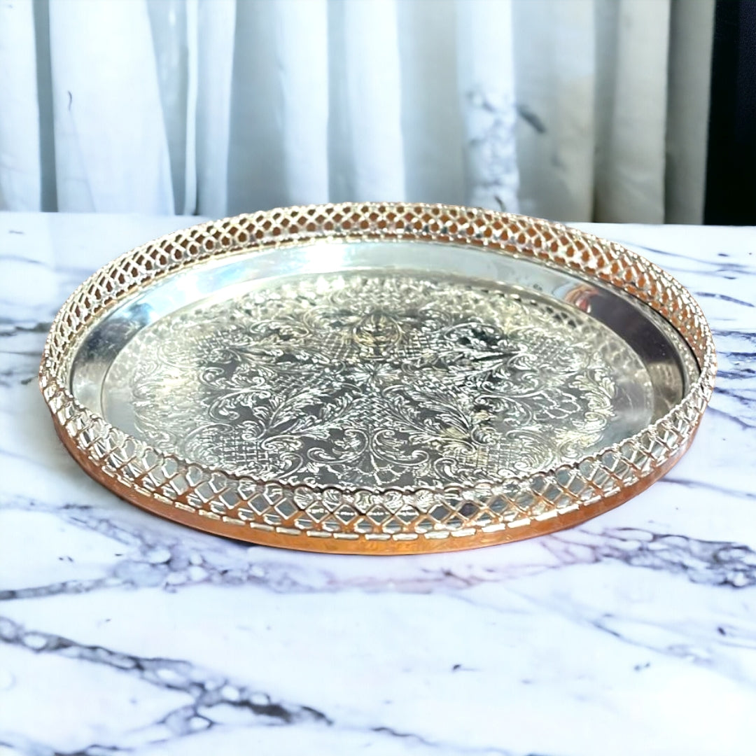 Bandeja Decorada redonda de metal plateado con diseño grabado y borde calado. Ideal para servir o decorar, mide 23xH4 cm.