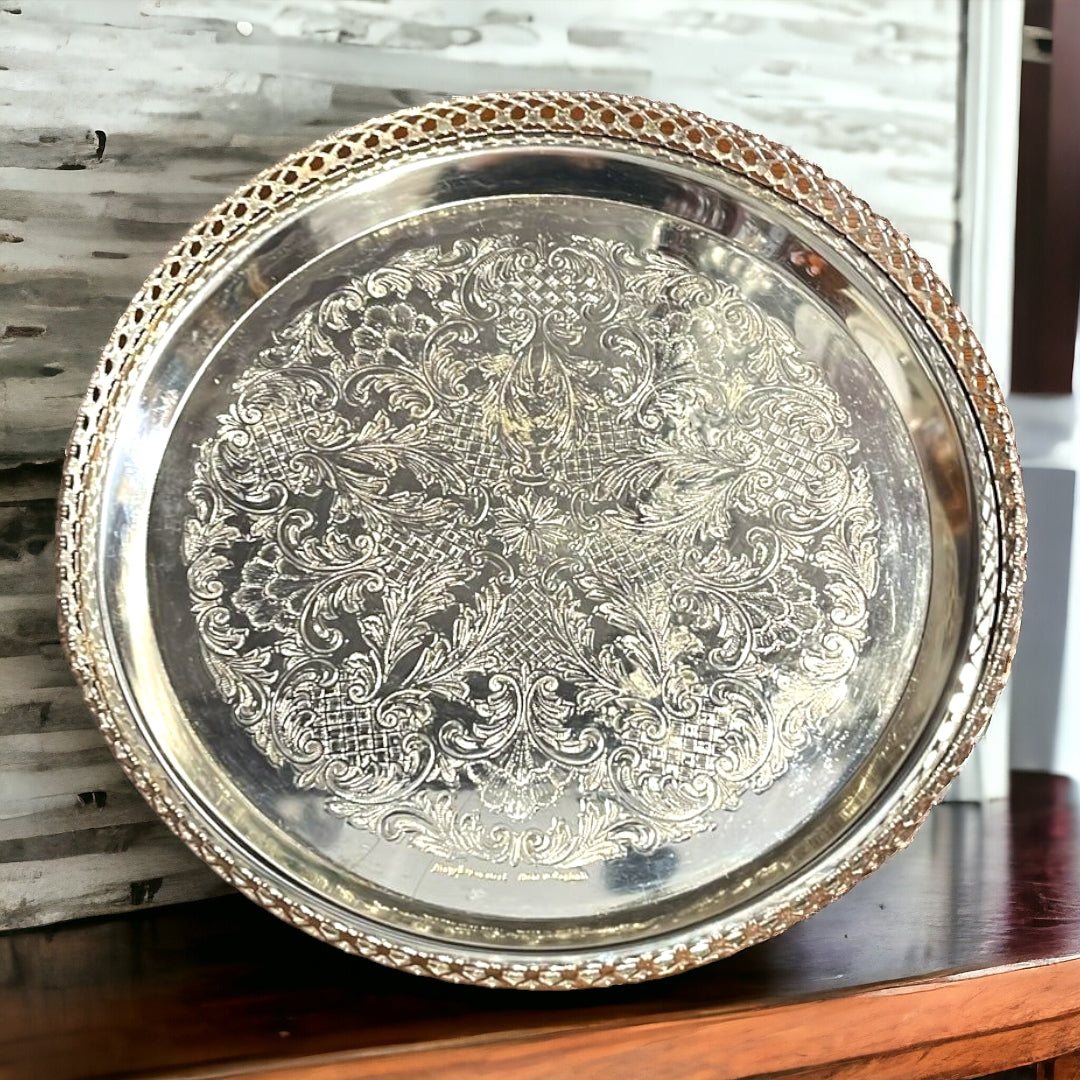 Bandeja Decorada redonda de metal plateado con diseño grabado y borde calado. Ideal para servir o decorar, mide 23xH4 cm.
