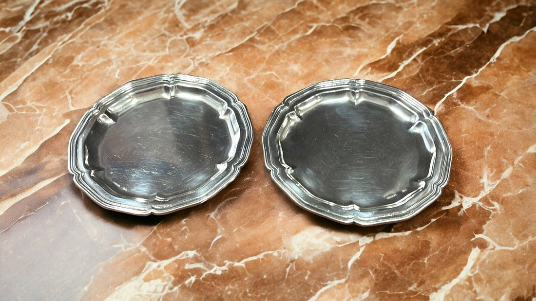 Platos decorativos de metal plateado con borde ondulado sobre superficie marmoleada. Añaden elegancia clásica a la decoración de mesa.