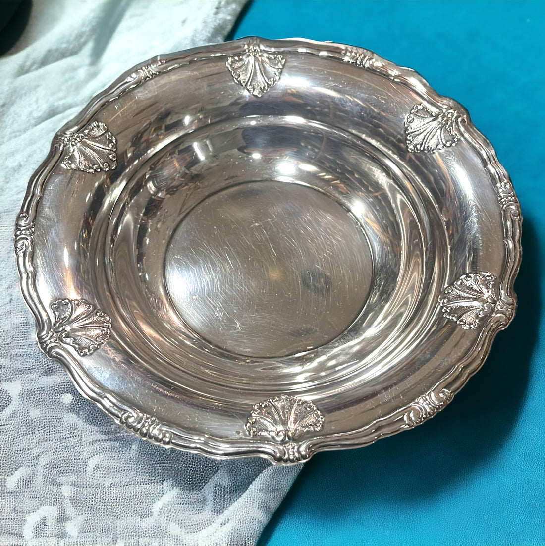 Plato redondo de metal plateado decorado con bordes en relieve, ideal para decoración de mesa elegante en hogar y eventos especiales.