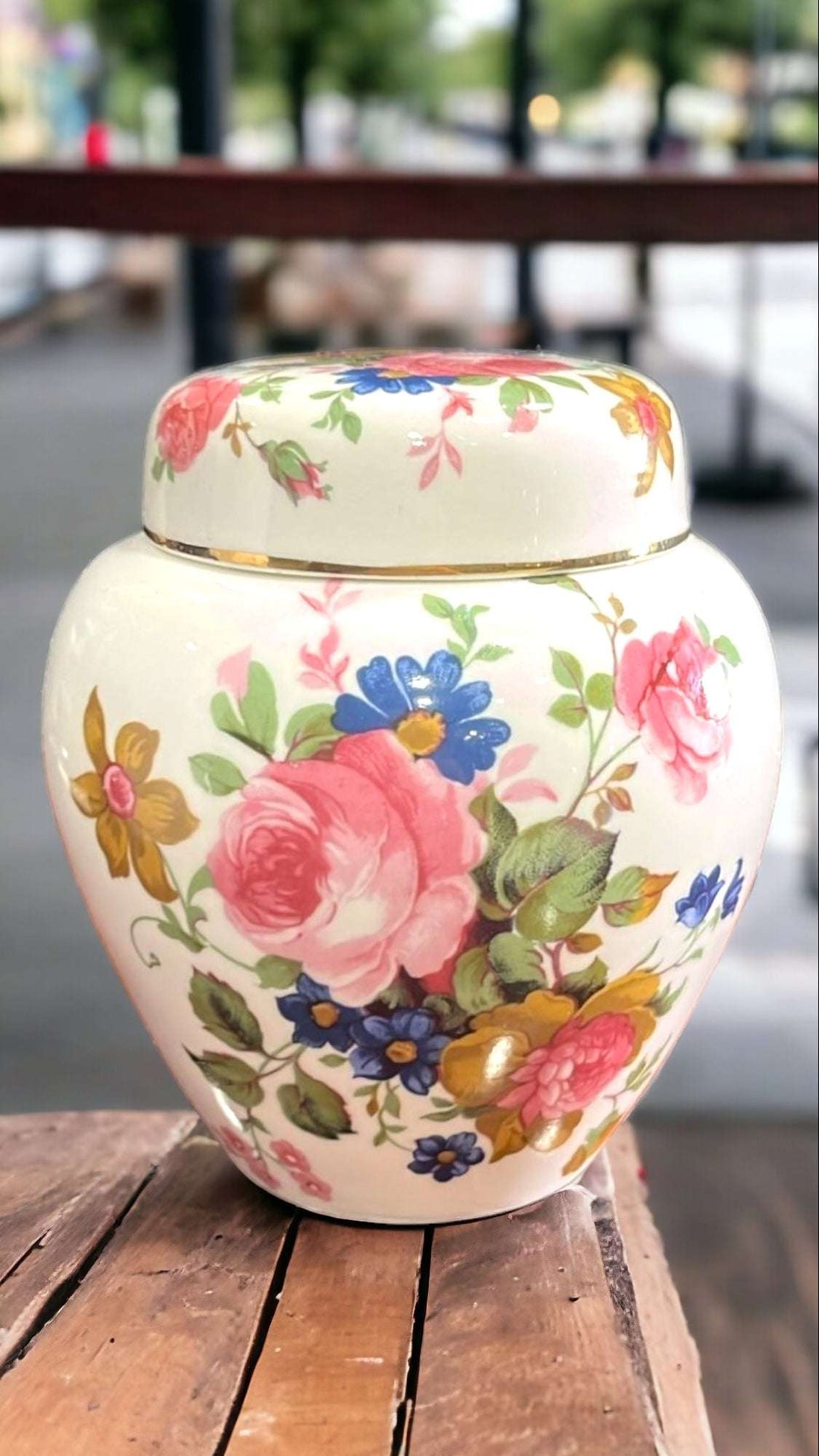 Tibor antiguo pintado a mano con motivos florales elegantes sobre fondo urbano. Decoración ideal para interiores clásicos o vintage.