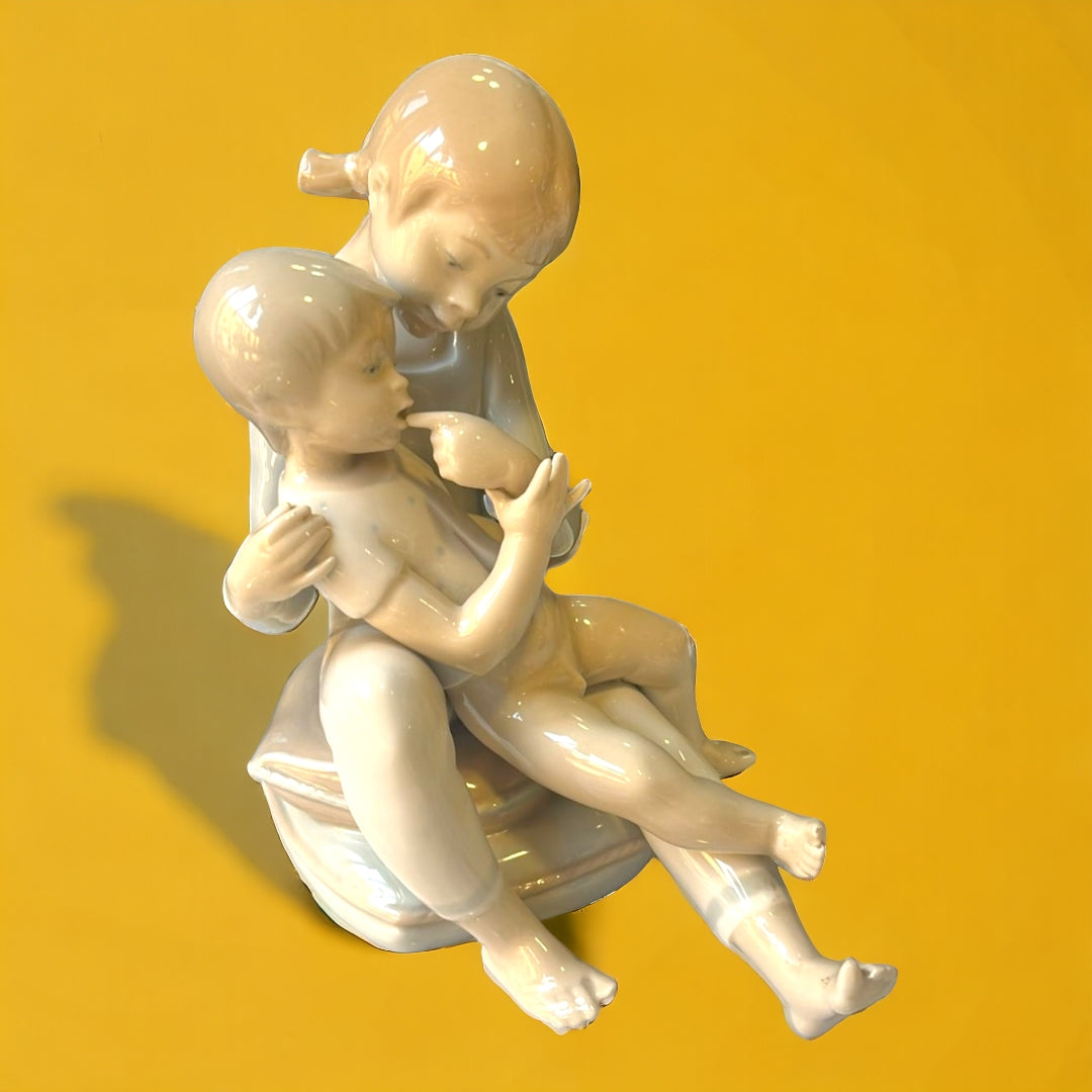 Figura de porcelana Hermanos Jugando de Lladró, representando a dos niños en un momento tierno. Elegancia y calidad para la decoración del hogar.