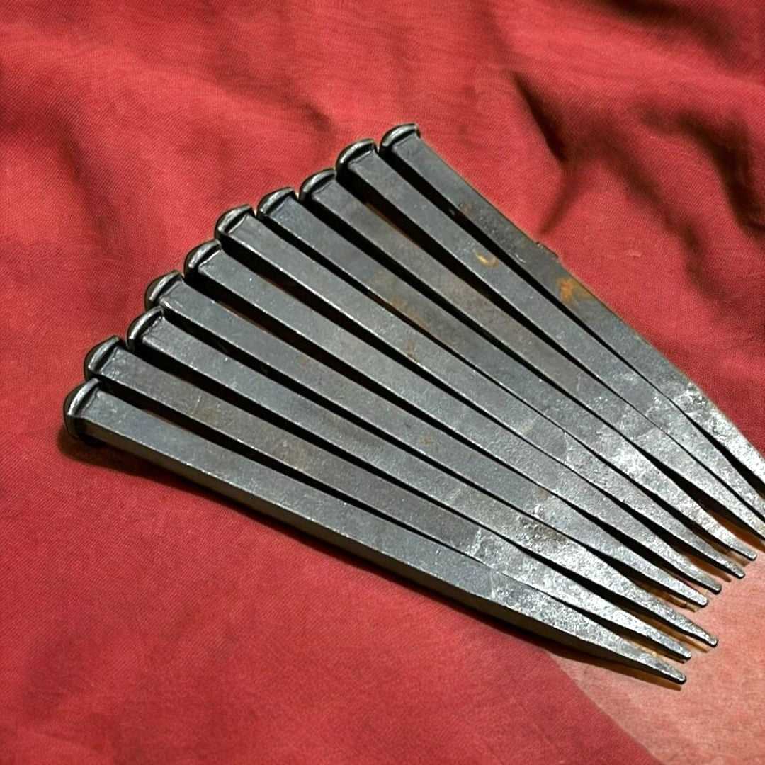 Juego de clavos grandes antiguos de hierro sobre tela roja, ideales para decoración rústica y restauración con estilo vintage.