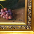 Firma de Adriana Ceballos en pintura al óleo de bodegón con sandías y uvas. Detalle artístico ideal para coleccionistas de arte clásico.