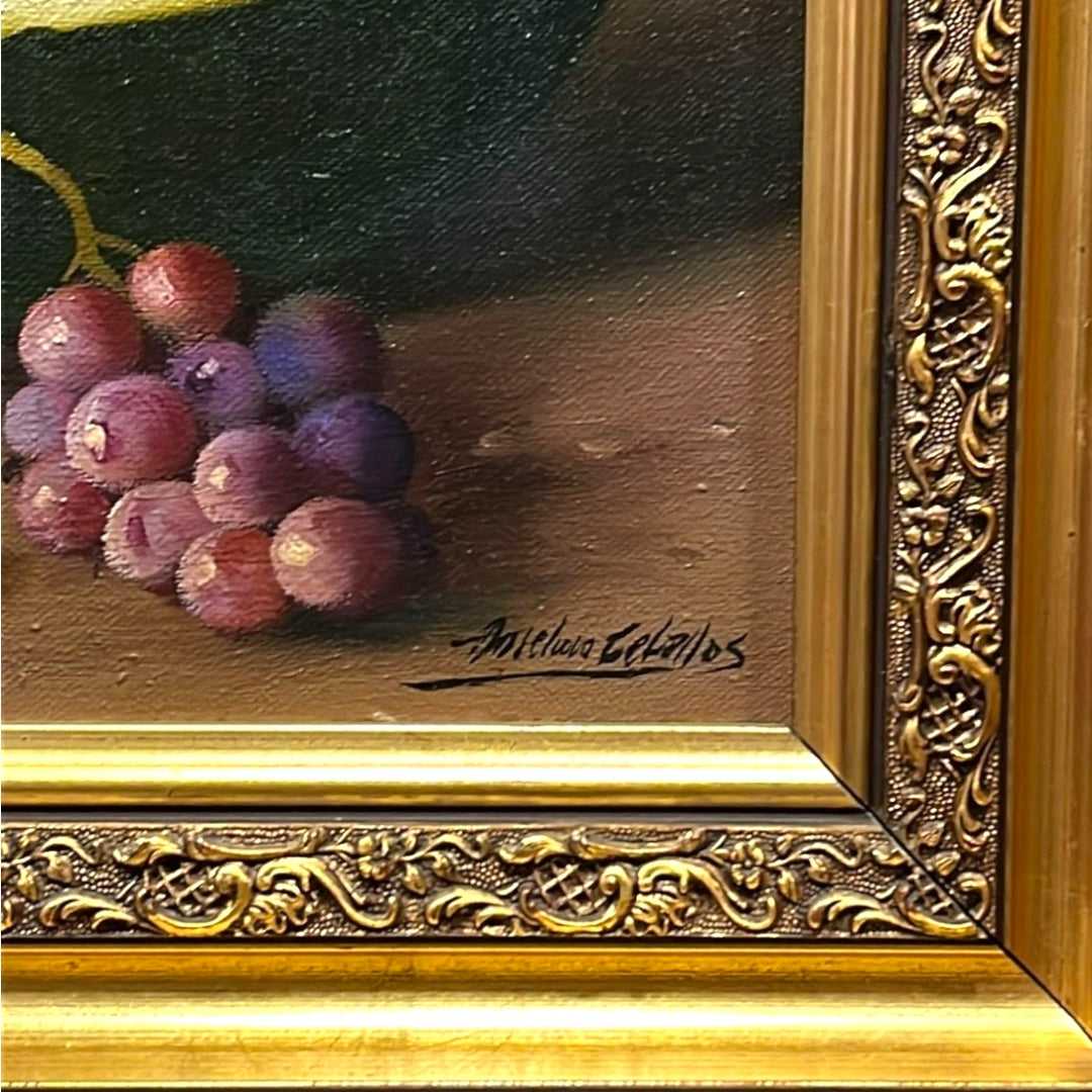 Firma de Adriana Ceballos en pintura al óleo de bodegón con sandías y uvas. Detalle artístico ideal para coleccionistas de arte clásico.