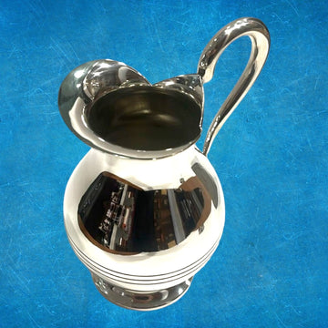 Jarra de metal plateado elegante con diseño moderno, acabado pulido y mango curvado, ideal para decoración o servir bebidas.