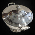 Sopera decorativa de metal plateado con acabado brillante, estilo clásico con tapa y asas, perfecta para decoración de interiores.