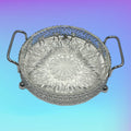 Plato entremesero de cristal con base de metal plateado y asas laterales. Diseño ornamental ideal para decoración de interiores clásicos.