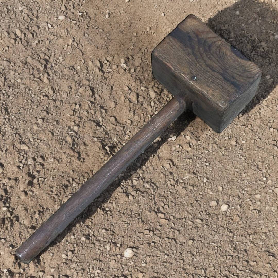 Antiguo mazo de madera rústico sobre tierra seca, pieza única y decorativa ideal para estilos vintage e industriales en decoración de hogar.