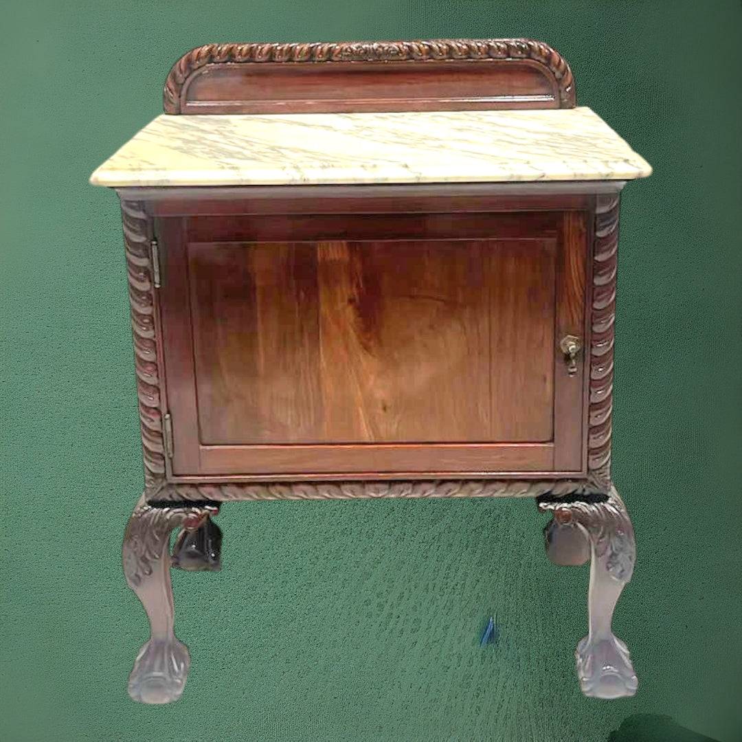 Mesita de noche antigua con tapa de mármol, elegante y funcional, con patas talladas y acabado en madera oscura. Ideal para decoración vintage de dormitorio.