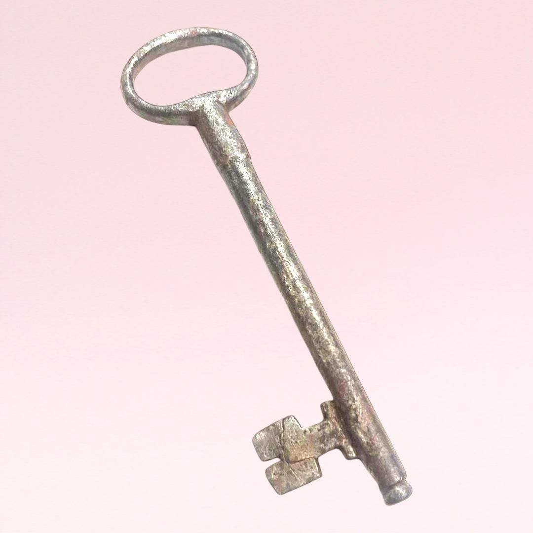 Llave antigua de forja para decoración con acabado envejecido sobre fondo rosa. Ideal para estilo rústico en espacios del hogar o jardín.