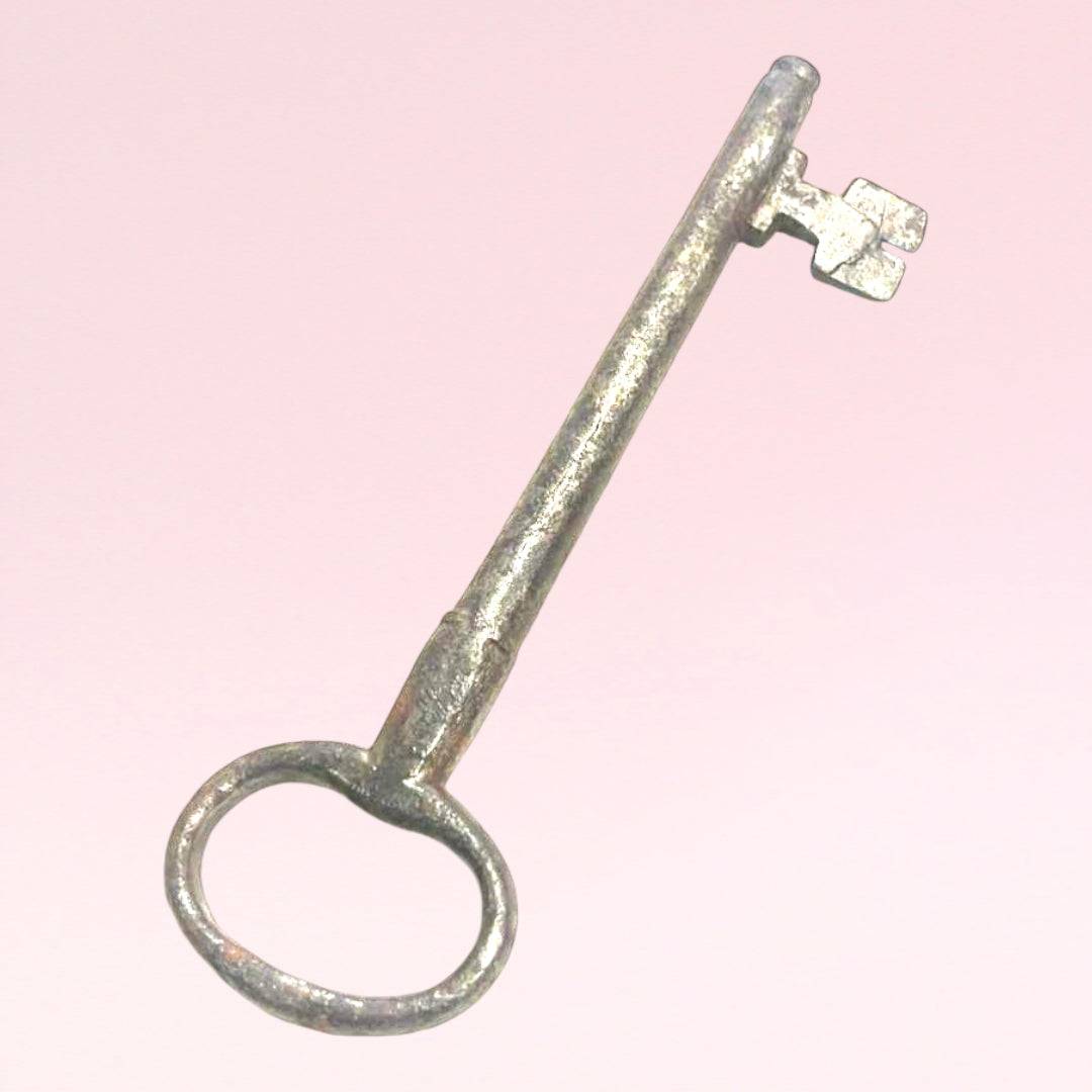 Llave antigua de forja para decoración con acabado envejecido sobre fondo rosa. Ideal para estilo rústico en espacios del hogar o jardín.