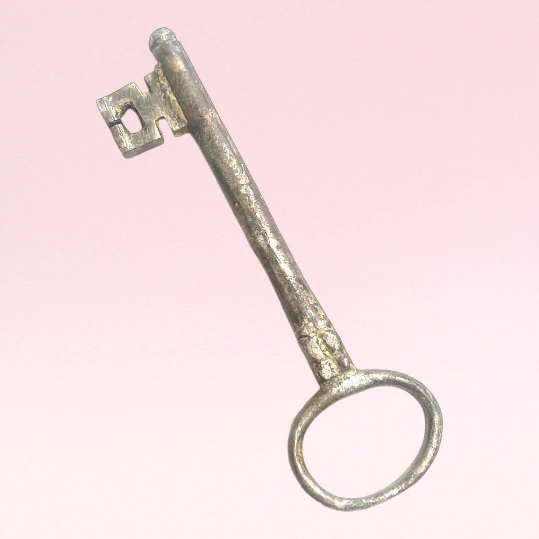 Llave antigua de forja en metal envejecido sobre fondo rosa, ideal como elemento decorativo único para tu hogar en estilo vintage.